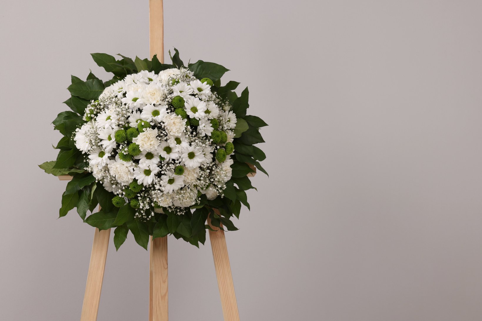 Funeral Wreath of Flowers on Wooden Stand against Grey Backgroun